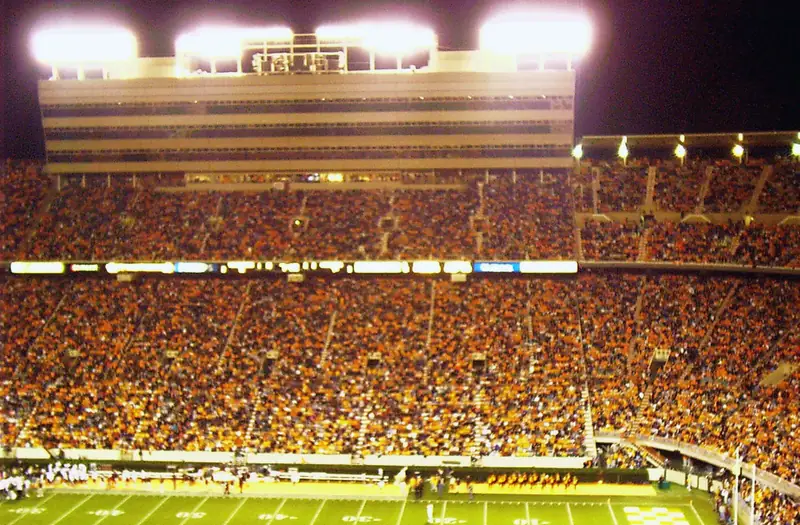 A packed college football stadium under the lights during a night game
