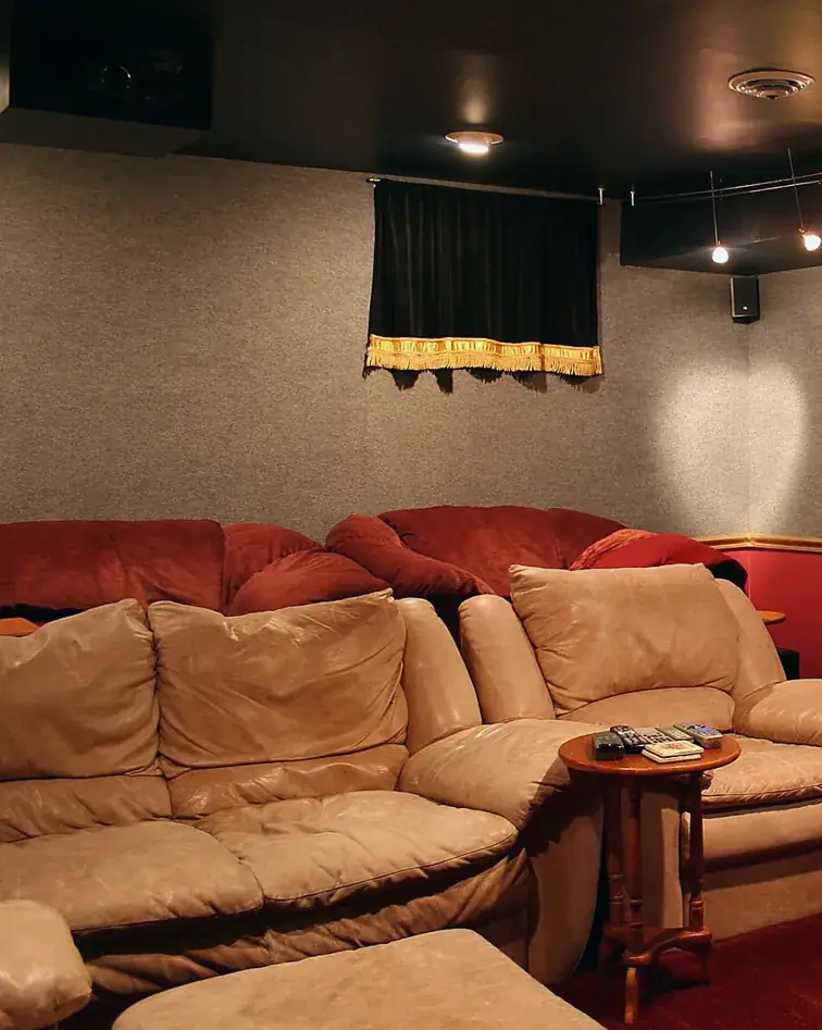 A basement media room with leather sofas and a side table covered in remote controls